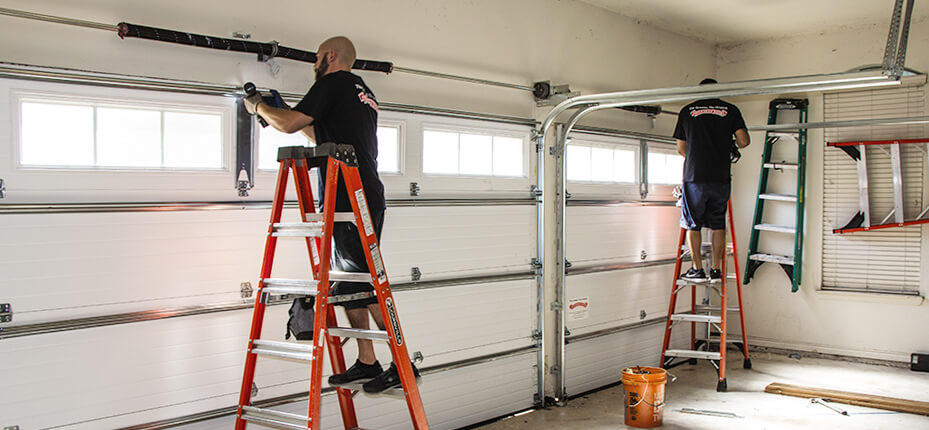 Two men on ladders work on garage door